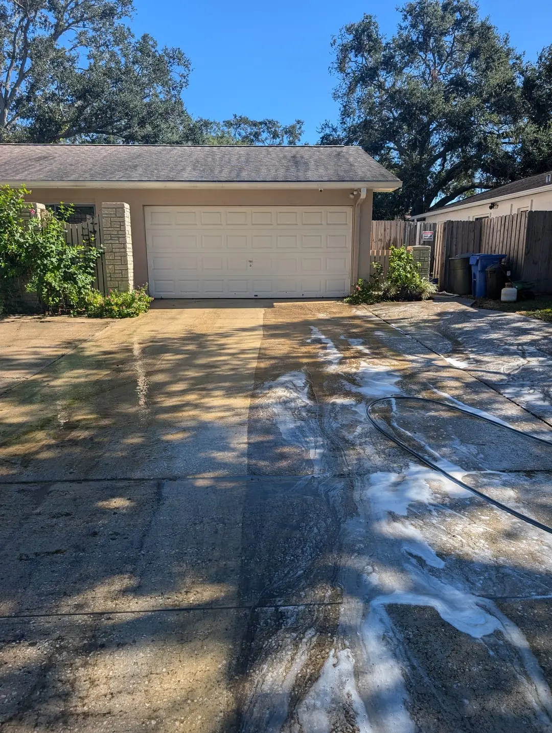 A residential driveway being pressure washed by Mr. Clean Cans — the cleaned side noticeably brighter than the untreated side